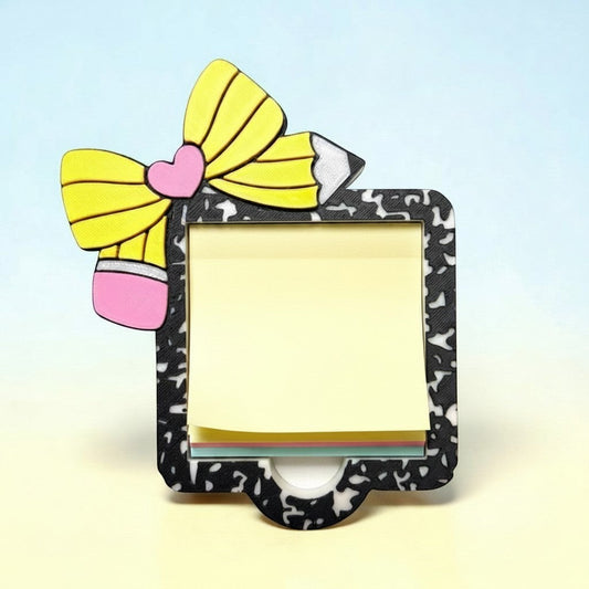 Xpress It Graphics 3D printed sticky note holder shaped like a yellow pencil with a pink heart and bow, black speckled frame, holding yellow lined notes.